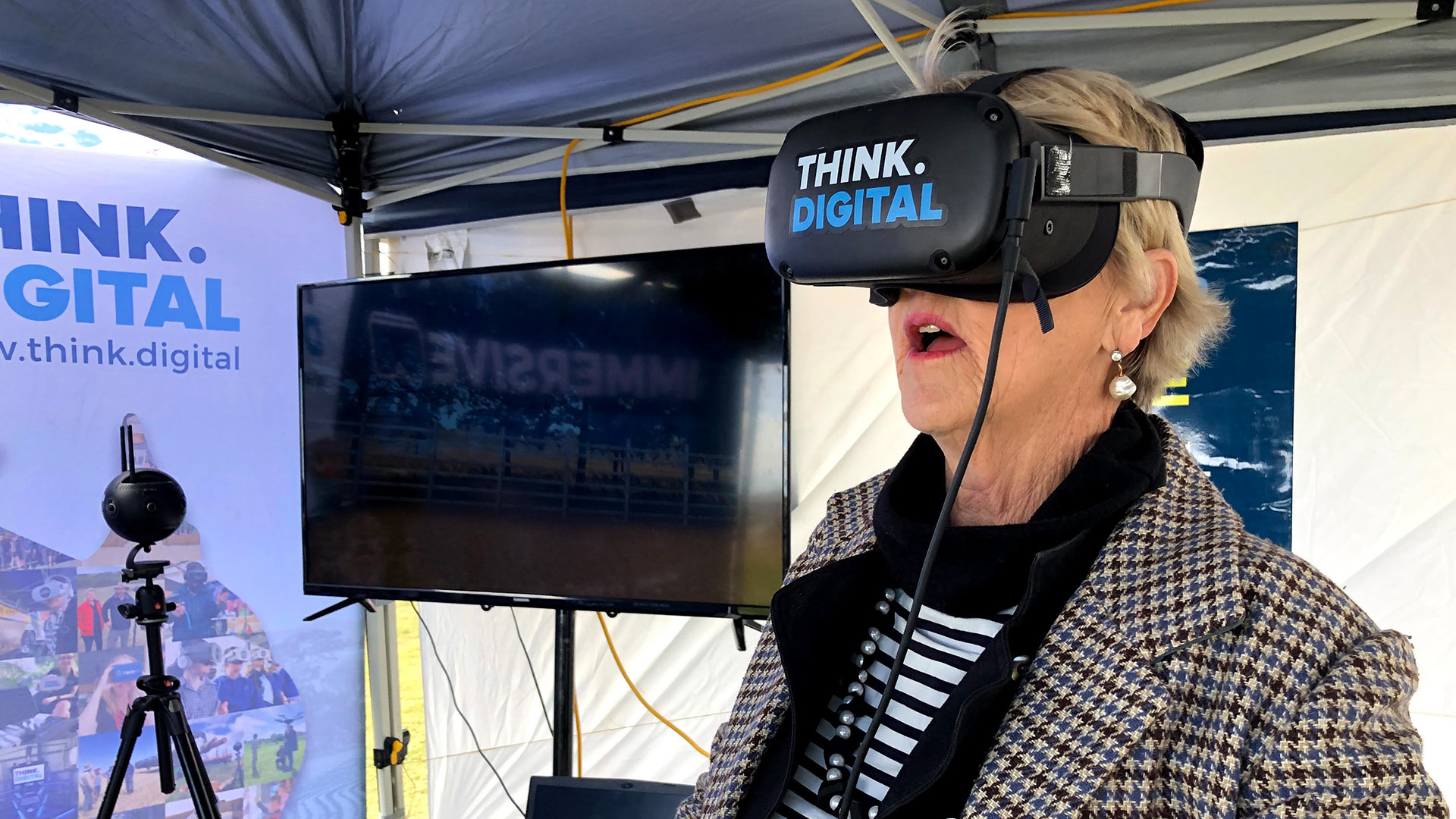 A woman wearing a "Think Digital" VR headset, visibly impressed with virtual reality.